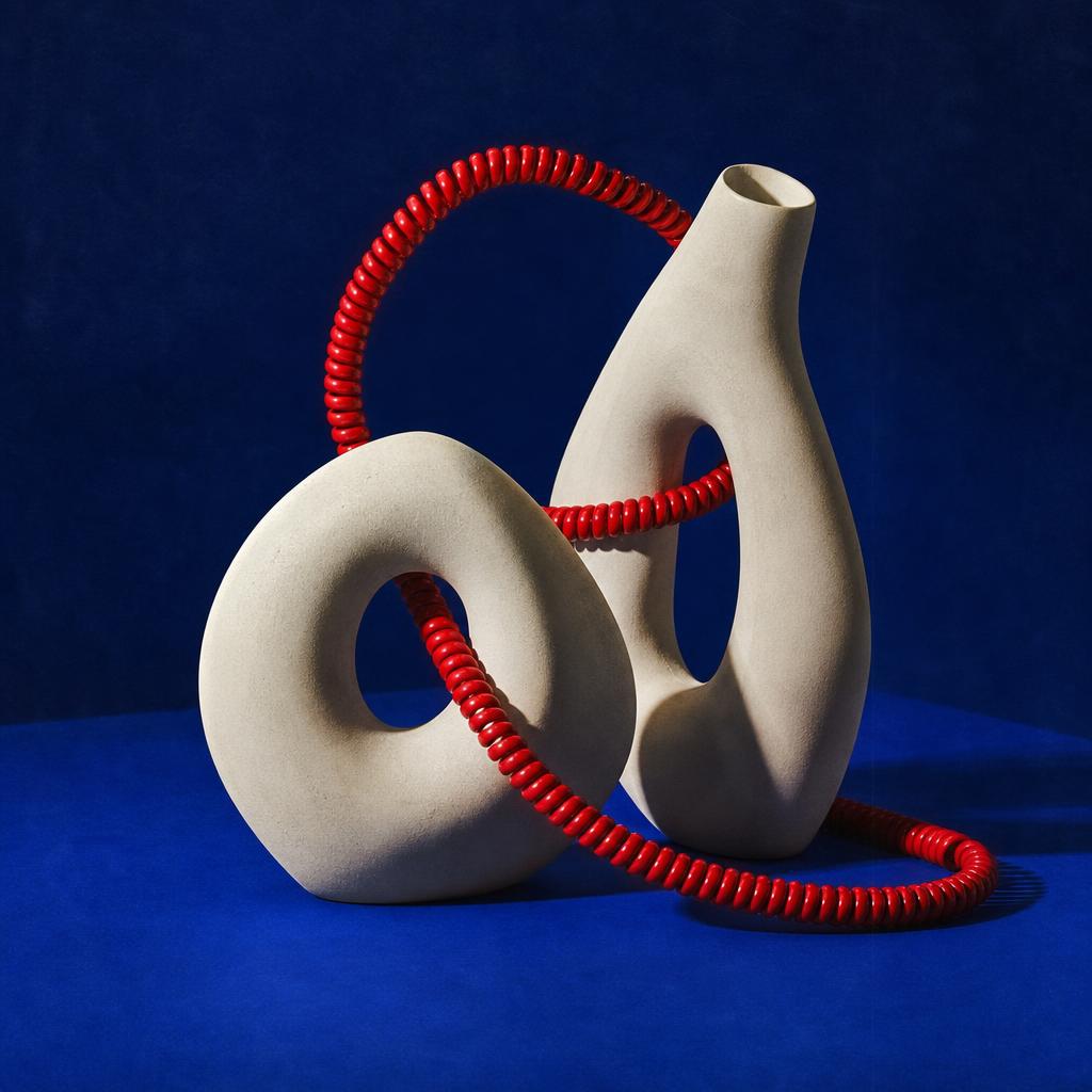 A glossy red loop weaving through ivory forms